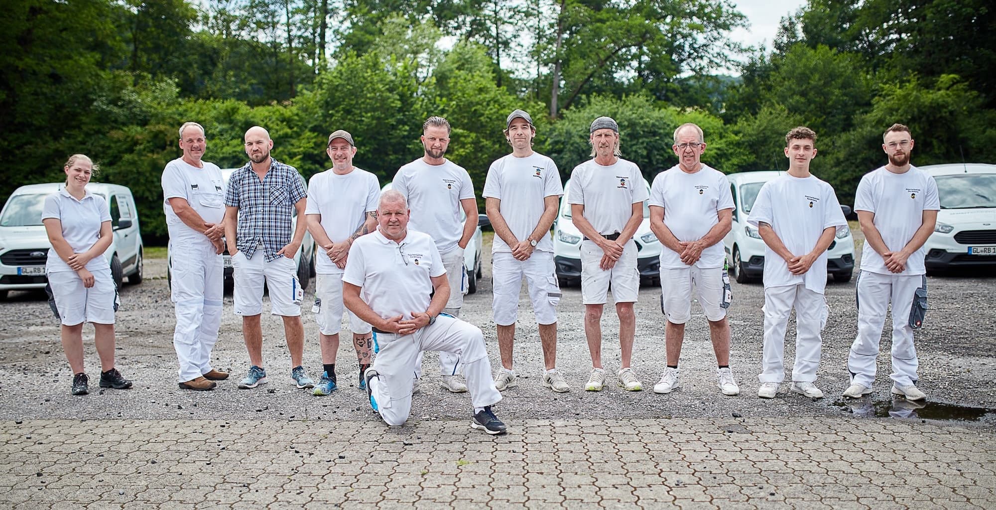 Team des Malerfachbetriebs Ralf Bardenberg in weißer Arbeitskleidung vor Firmenfahrzeugen