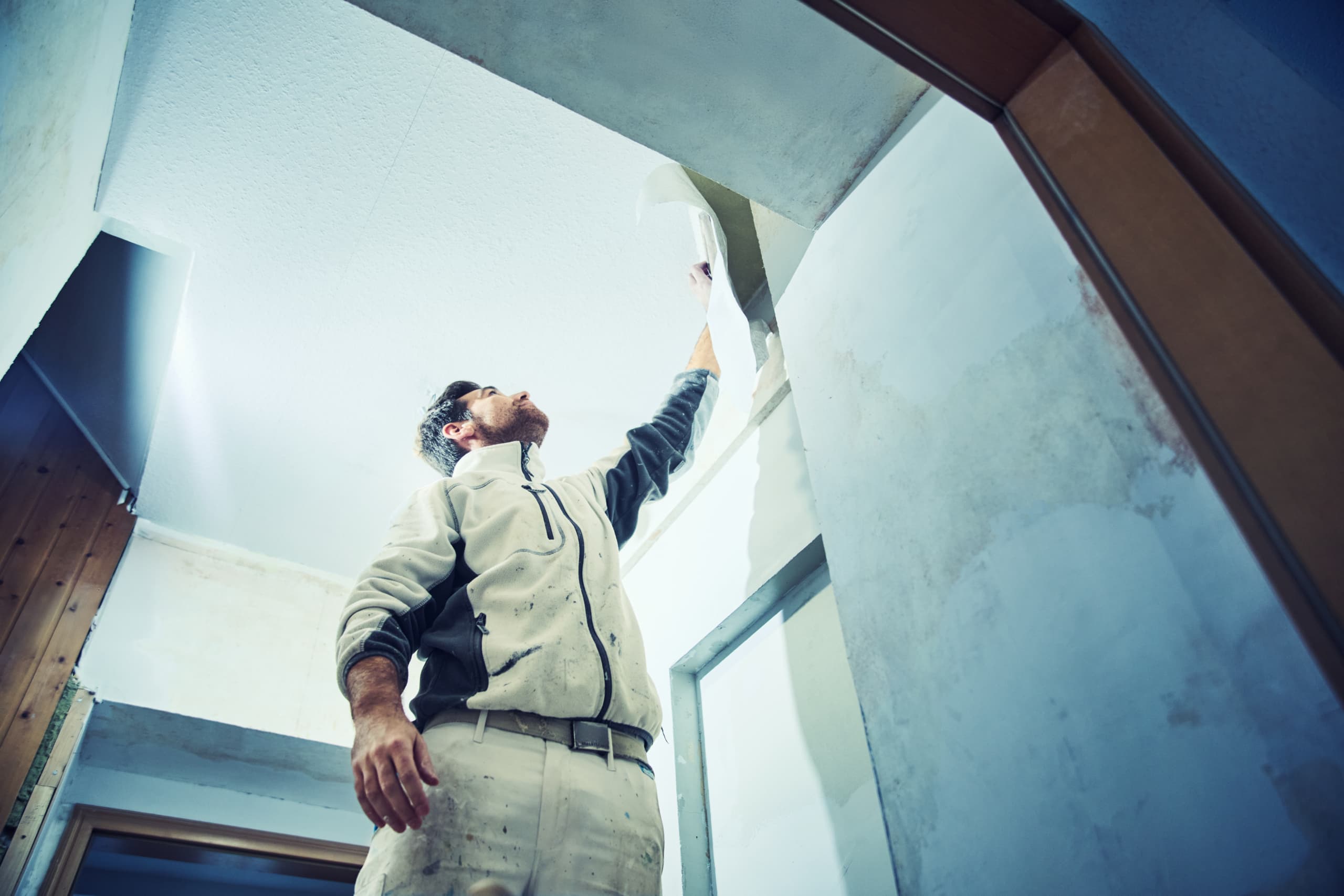 Maler in Arbeitskleidung verputzt eine Wand im Innenraum