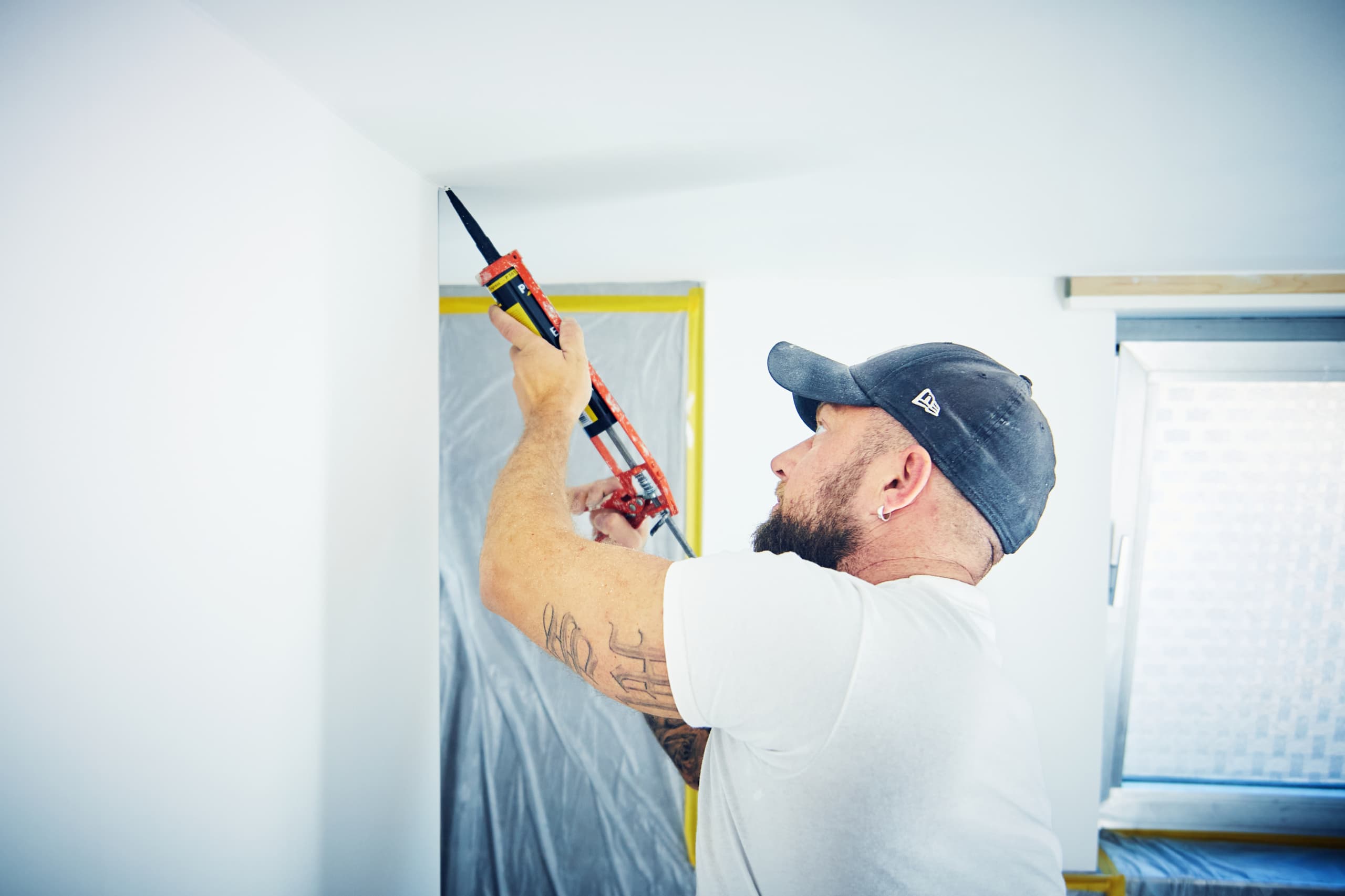 Maler trägt Silikonfuge an der Decke einer abgeklebten Baustelle auf
