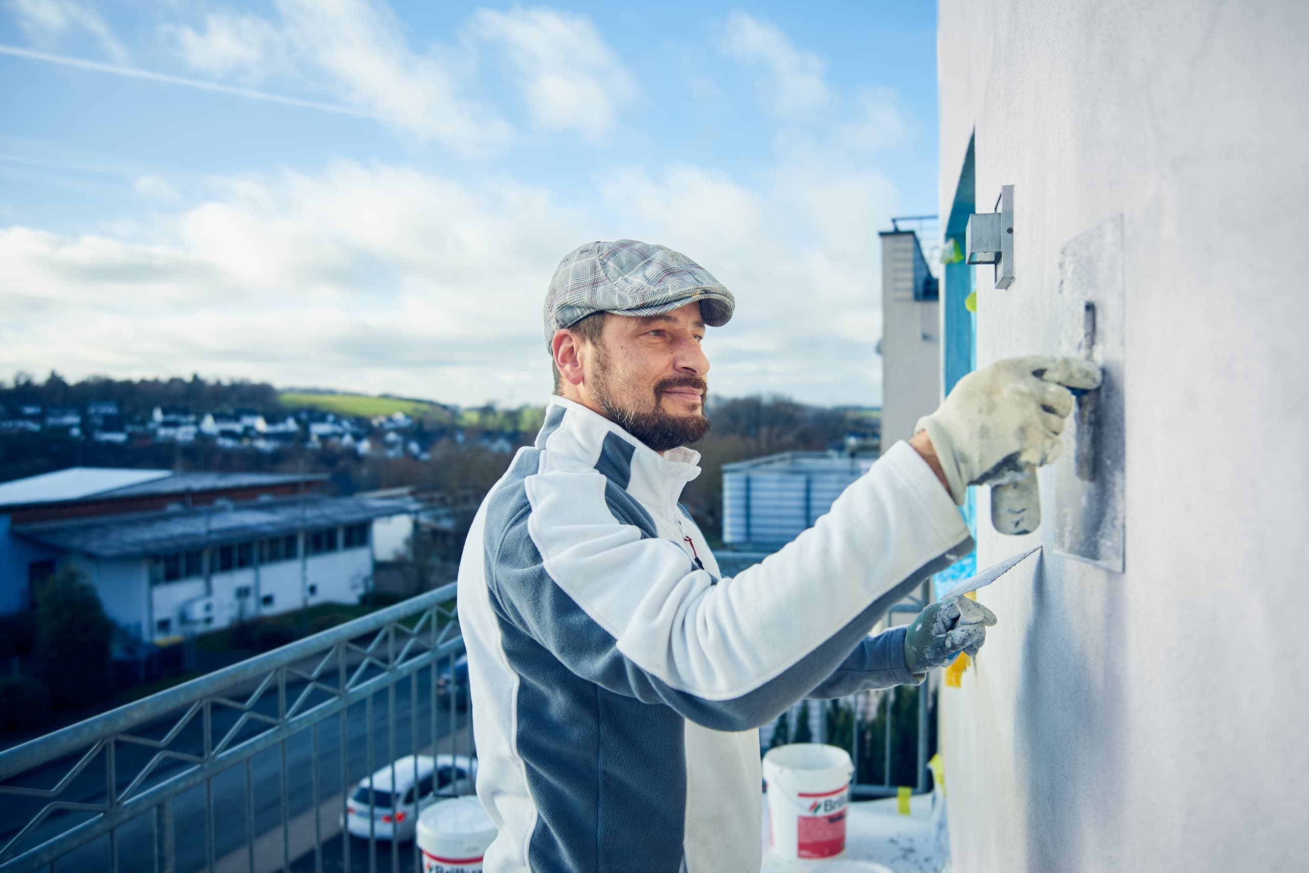 Maler in Arbeitskleidung verputzt eine Fassade mit Blick über das Bergische Land