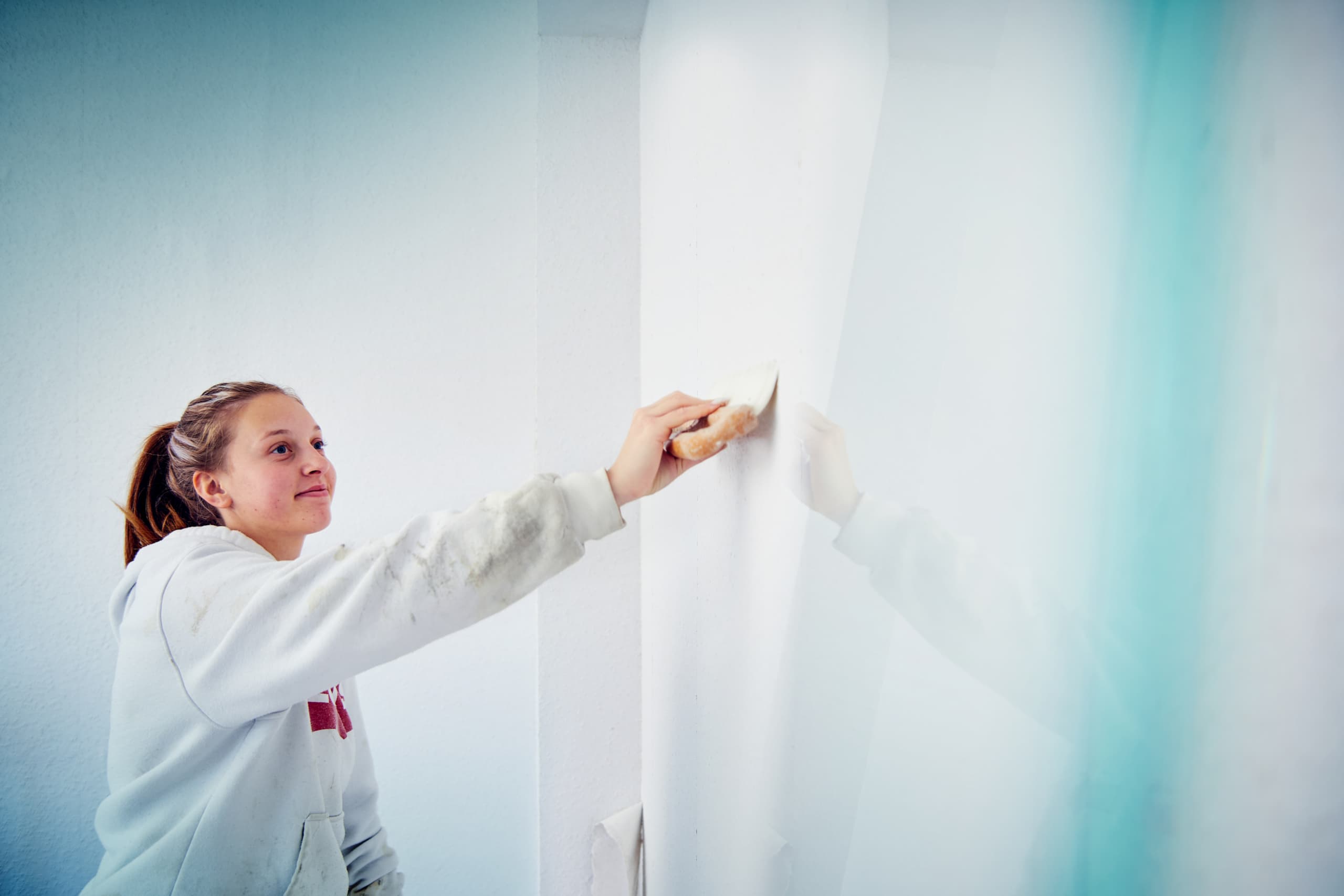 Junge Malerin glättet eine frisch tapezierte weiße Wand